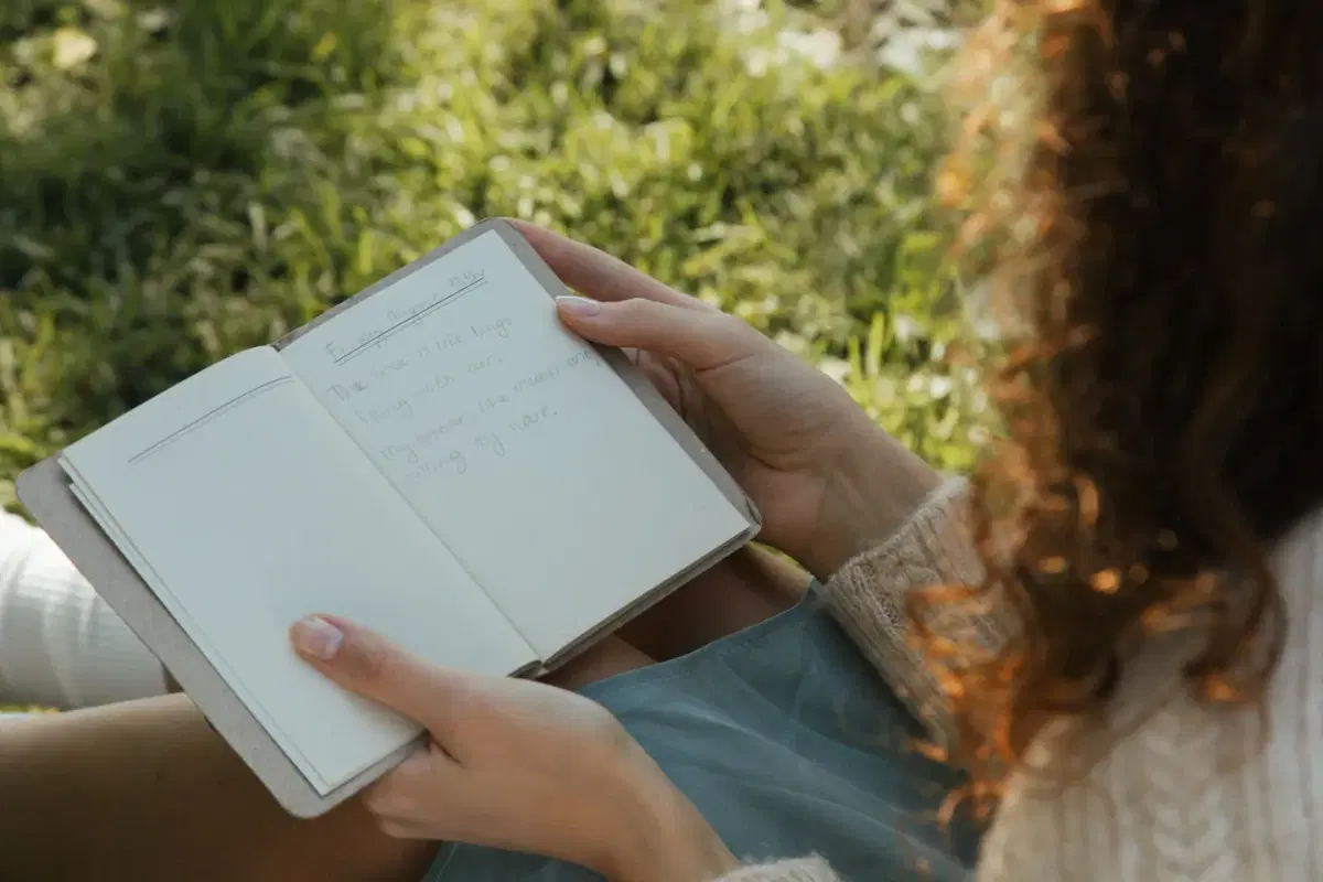 An adult holding an open journal outdoors.